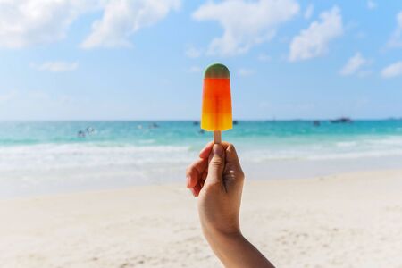 Ice cream stick in hand with sea background / Colorful ice cream fruit on beach in summer hot weather ocean landscape nature outdoor vacationの写真素材