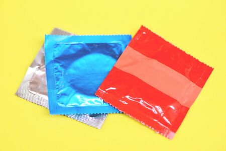 Condom isolated on yellow background / Colorful condom pack for birth control contraceptive means prevent pregnancy or sexually transmitted diseaseの写真素材
