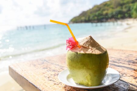 Coconut tropical fruit on table and sand beach background water / Fresh coconut juice summer with flower on beach sea in hot weather ocean landscape nature outdoor vacation , young coconutの写真素材
