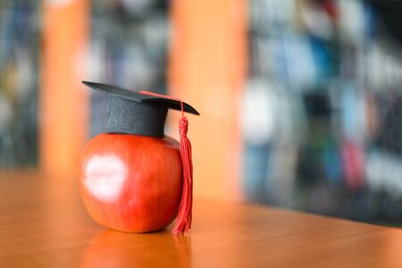 Education learning concept / Graduation cap on apple on the table with bookshelf in the library...