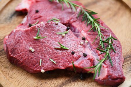 Raw beef meat rosemary on wooden cutting board on the kitchen table for cooking beef steak roasted...