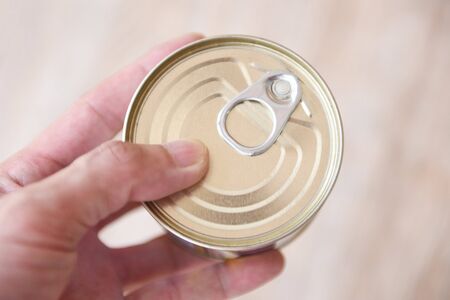 Canned food metal cans in hand / canned goods non perishable food storage goods in kitchen home or for donationsの写真素材