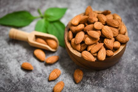 Almonds nuts on wooden bowl with leaf almonds top view on dark background / Roasted almond for snackの写真素材