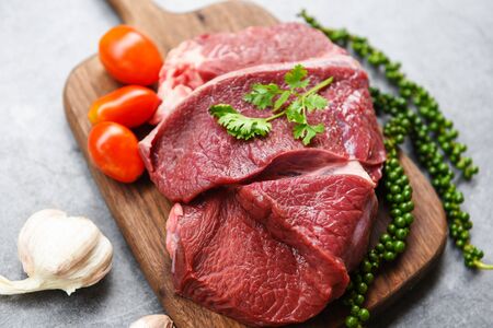 Raw beef meat on wooden cutting board on the kitchen table for cooking beef steak roasted or grilled with ingredients herb and spices , Fresh beef animal proteinの写真素材
