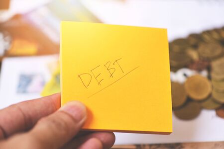 Debt concept with write debt on paper in hand and coins on table backgroundの写真素材