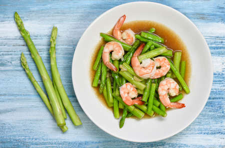 Stir fried shrimps with asparagus green on white plate and wooden table background / Asparagus...