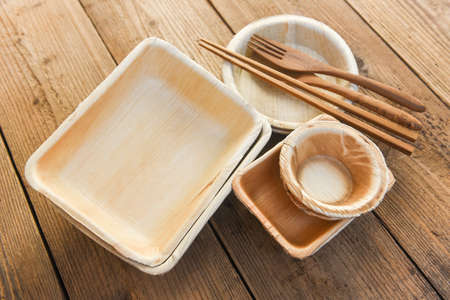 Natural eco-friendly food packaging disposable utensils with dish plate bowl cup and wooden fork spoon / Eco friendly disposable tableware from palm leaf or betel nut , zero waste environment conceptの写真素材