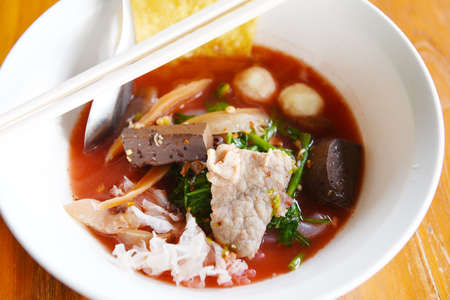 Noodles with seafood on red soup / hot and spicy thai food noodle squid pork fish ball morning glory crispy wonton skin pork and blood cubesの写真素材