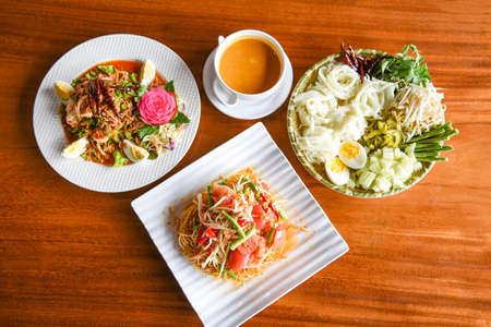 Asian Thai food top view with Thai rice noodles , curry Papaya salad , shrimp salad food served on wooden table setting plateの写真素材