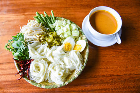 Thai rice noodles / Close up Thailand food vermicelli noodle boiled eggs and fresh vegetables on plate with curry soup bowl served wooden tableの写真素材