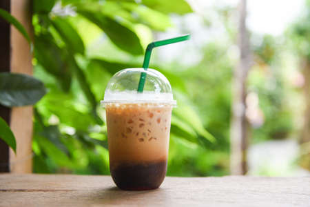 Iced coffee latte in plastic cup on wooden table and nature green background / iced drinks