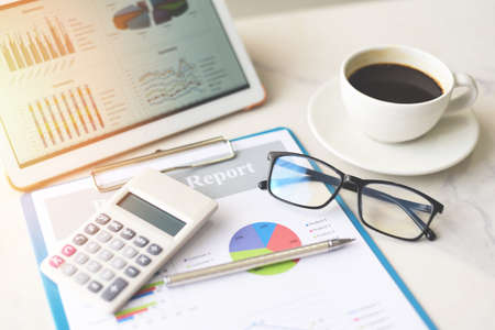 Business graphs chart on a tablet computer technology on the table with coffee cup on desk and...