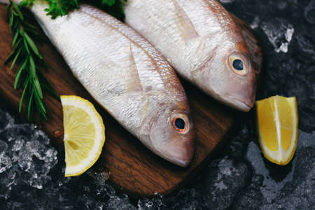 Fresh raw fish with ingredients lemon rosemary and lettuce for making cooked food on ice at market sea bream seafood fish frozenの写真素材