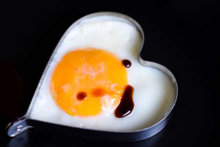 Fried eggs in a frying pan with sauce for breakfast on a black background / Fried egg for a healthy...