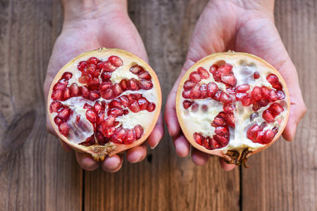 Pomegranate fruit cut half on hand, ripe pomegranate with seeds on wooden table backgroundの写真素材