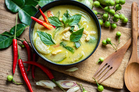 Chicken green curry Thai food on soup bowl with ingredient vegetable herbs and spices pepper chili on wooden table background, Traditional green curry chicken cuisine asian food. Top viewの写真素材