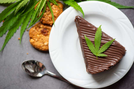 Chocolate cake and cookies with cannabis leaf - marijuana leaves plant on white plate on the wooden...