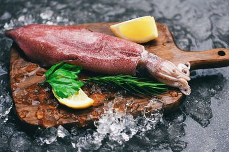 Fresh squids octopus or cuttlefish for cooked food salad restaurant, Raw squid on ice wooden cutting board with lemon parsley on the dark plate seafood marketの写真素材
