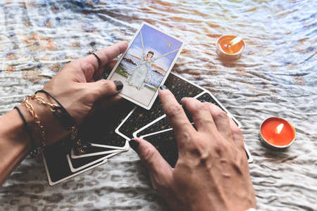 Show fortune tellers of hands holding tarot cards and tarot reader with candle light on the table, Performing readings magical performances, Things mystical astrologists forecasting conceptの写真素材