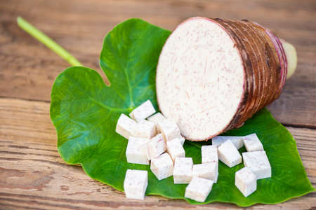 Taro root with half and slice cubes on taro leaf and wooden background, Fresh raw organic taro root ready to cookの写真素材