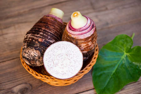 Taro root with slice half on basket and taro leaf and wooden background, Fresh raw organic taro root ready to cookの写真素材