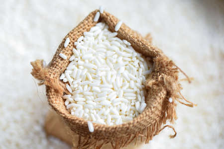 Jasmine white rice in sack and harvested rice on wooden table, harvest rice and food grains cooking conceptの写真素材
