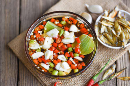 fish sauce on white bowl and fresh chili garlic lemon lime and small dried fish on sack, fish sauce...