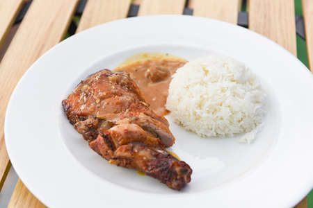 Thai rice food, cooked white rice and grilled chicken with sauce on white plate and wooden table background, Spicy bbq chicken legs grilledの写真素材