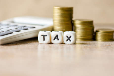Block word tax with money and calculator on wooden background, TAX and stacked coins financial Tax concept.の写真素材