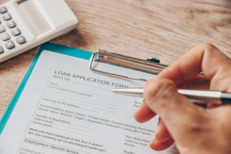 Personal loan concept with loan application form paper with calculator and business manholding a penclient signs loan on the table, Loan business finance economy commercial real estate investments.の写真素材