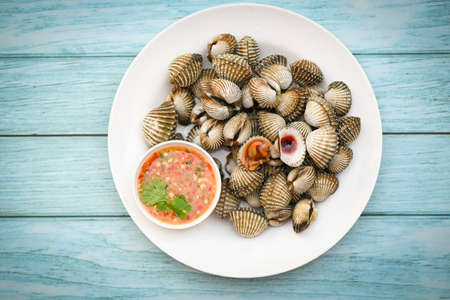 Fresh raw shellfish blood cockle ocean gourmet seafood in the restaurant, Cockles on white plate with seafood sauce on table background - top viewの写真素材