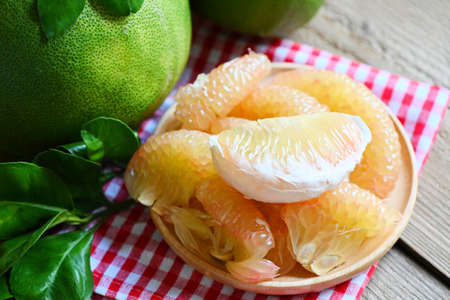 fresh green pomelo peeled and leaf frome pomelo tree , pummelo , grapefruit in summer tropical fruit  in thailand , pomelo fruit on wooden plate backgroundの写真素材