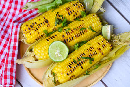 sweet corn cooked on wooden background, ripe corn cobs grilled sweetcorn for food vegan dinner or snack, sweet corn food with lime and coriander - top viewの写真素材