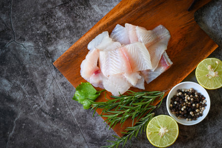 fish fillet on wooden board with ingredients for cooking, fresh raw pangasius fish fillet with herb...