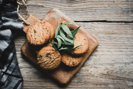 Cannabis food cookies with cannabis leaf marijuana herb on wooden background, delicious sweet dessert cookie with hemp leaf plant THC CBD herbs food snack and medical concept - top viewの写真素材