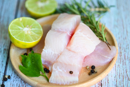 Fish fillet on wooden plate with ingredients celery for cookin, fresh raw pangasius fish fillet with lemon lime, meat dolly fish tilapia striped catfish - top viewの写真素材