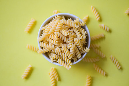 Pasta raw macaroni on yellow background, close up raw macaroni spiral pasta uncooked delicious whole grain fusilli pasta for cooking foodの写真素材