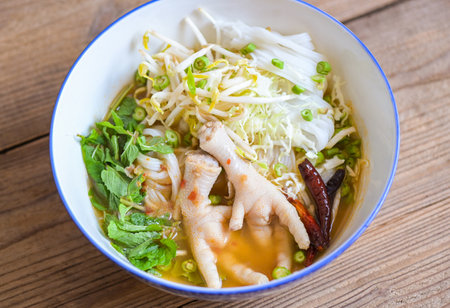 Rice noodles with chicken feet on soup bowl on wooden table food background - Thai food thai rice noodles spicy soup curry with fresh vegetableの写真素材