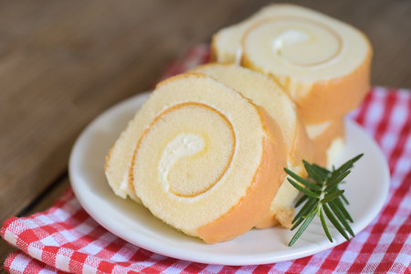 sponge cake roll slices sweets dessert cream roll vanilla snacks and food concept - Swiss Roll Cake, Cake roll on plate cake with rosemary on tableの写真素材