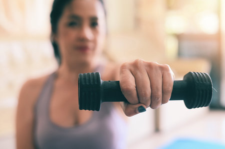 sporty woman exercise muscles in sportswear with dumbbell at home in the living room, woman exercising at home, woman dumbbells in her hands, sport recreation health care conceptの写真素材