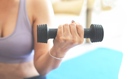 woman exercising at home, woman dumbbells in her hands, sporty woman exercise muscles in sportswear with dumbbell at home in the living room, sport recreation health care conceptの写真素材