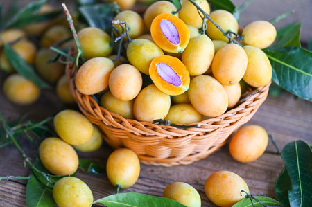 Marian plum fruit and leaves in basket on wooden background, tropical fruit Name in Thailand Sweet Yellow Marian Plum Maprang Plango or Mayong chidの写真素材