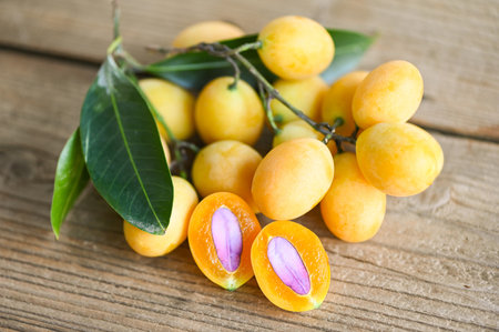 Marian plum fruit and leaves in plate on wooden background, tropical fruit Name in Thailand Sweet Yellow Marian Plum Maprang Plango or Mayong chid - top viewの写真素材