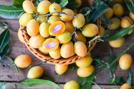 Marian plum fruit and leaves in basket on wooden background, tropical fruit Name in Thailand Sweet Yellow Marian Plum Maprang Plango or Mayong chidの写真素材