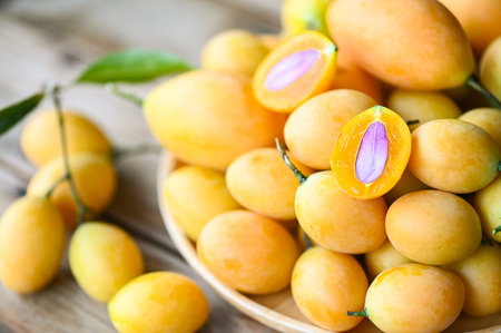 tropical fruit Name in Thailand Sweet Yellow Marian Plum Maprang Plango or Mayong chid, Marian plum fruit and leaves in plate on wooden backgroundの写真素材