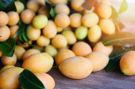 Marian plum fruit and leaves in plate on wooden background, tropical fruit Name in Thailand Sweet Yellow Marian Plum Maprang Plango or Mayong chidの写真素材