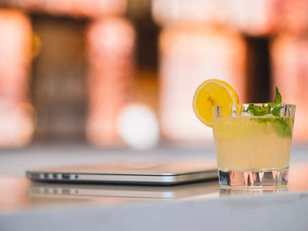 a glass of cocktail and laptop on a bar tableの写真素材
