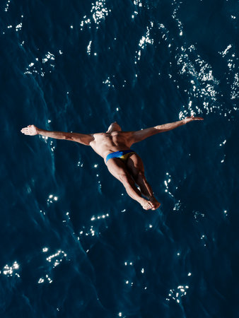 a professional male diver is jumping off a cliff into the sea
