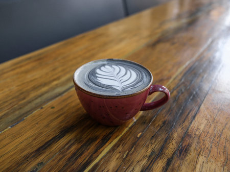 Fresh latte coffee in red mug on rustic tableの写真素材