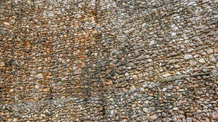 Large ancient wall of multicolor stones. Bushes of grass crawled out of the crevicesの写真素材